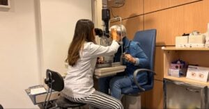Optometrist examining a patient's eyes with a slit lamp in a bright exam room